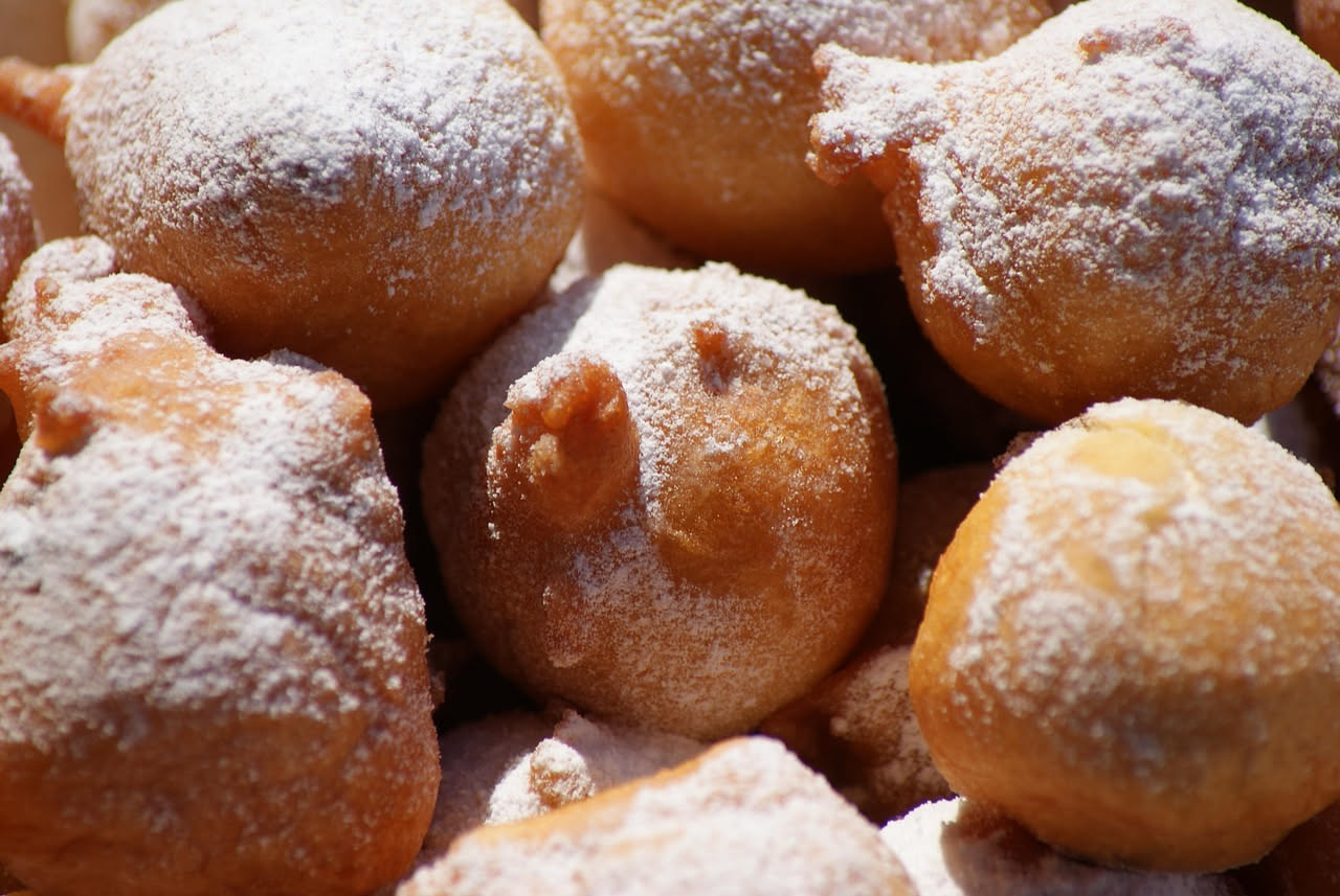 Sfinciuni di ricotta dorati poggiati su un piatto bianco, ricoperti di zucchero granulato, con uno tagliato a meta che mostra il ripieno di ricotta cremosa all interno