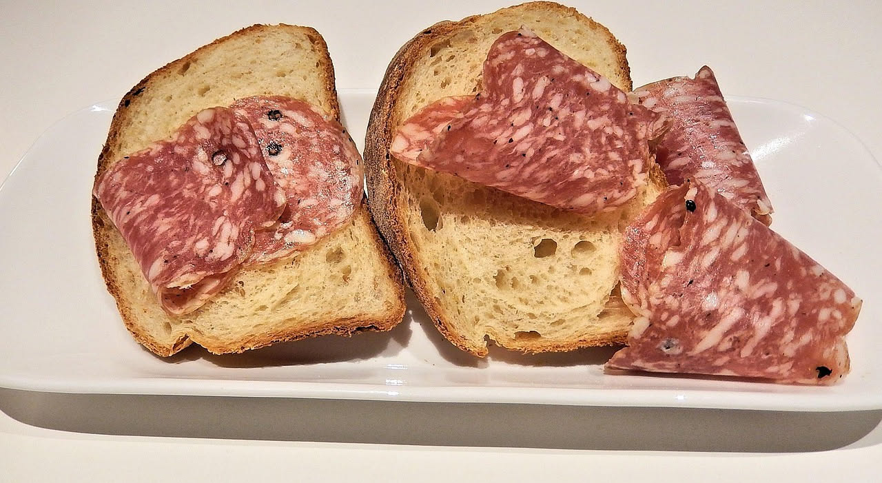 Soppressata affettata sottile su un tagliere di legno con coltello da affettare, bacche di pepe visibili sulla superficie del salume