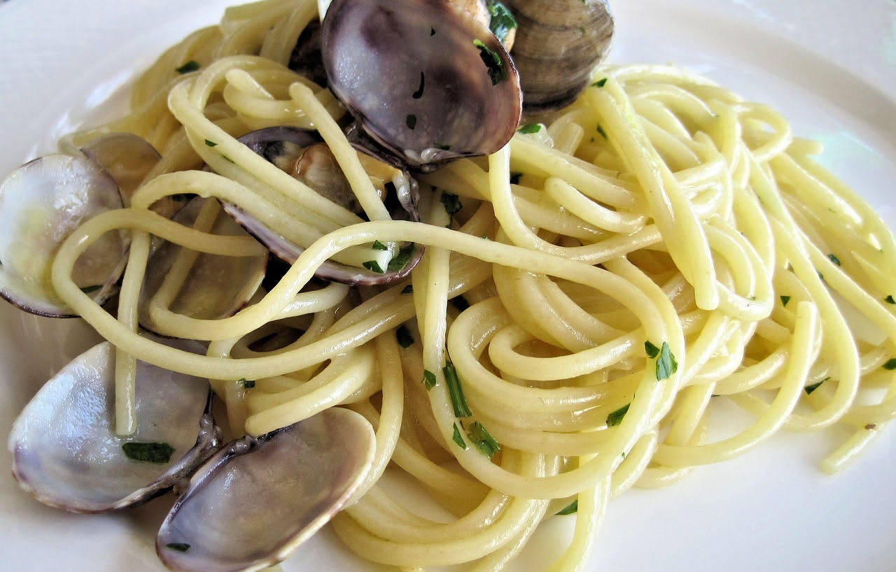 Spaghetti alle vongole veraci in piatto bianco con vongole aperte sparse fra la pasta, prezzemolo fresco e gocce d olio extravergine
