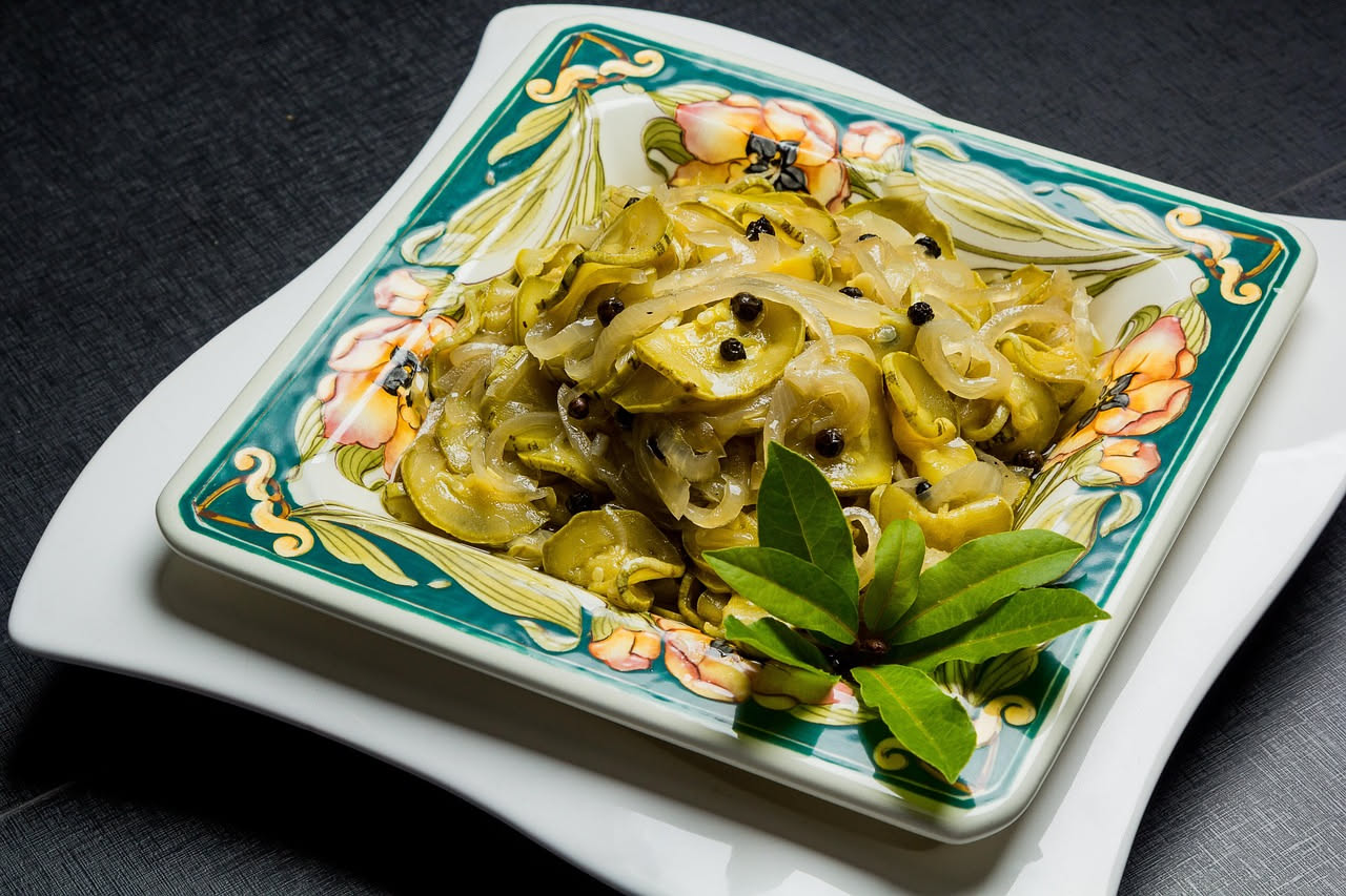 Zucchine tagliate a rondelle dorate, lucide di glassa agrodolce, in un piatto bianco con fondo sfocato di cucina