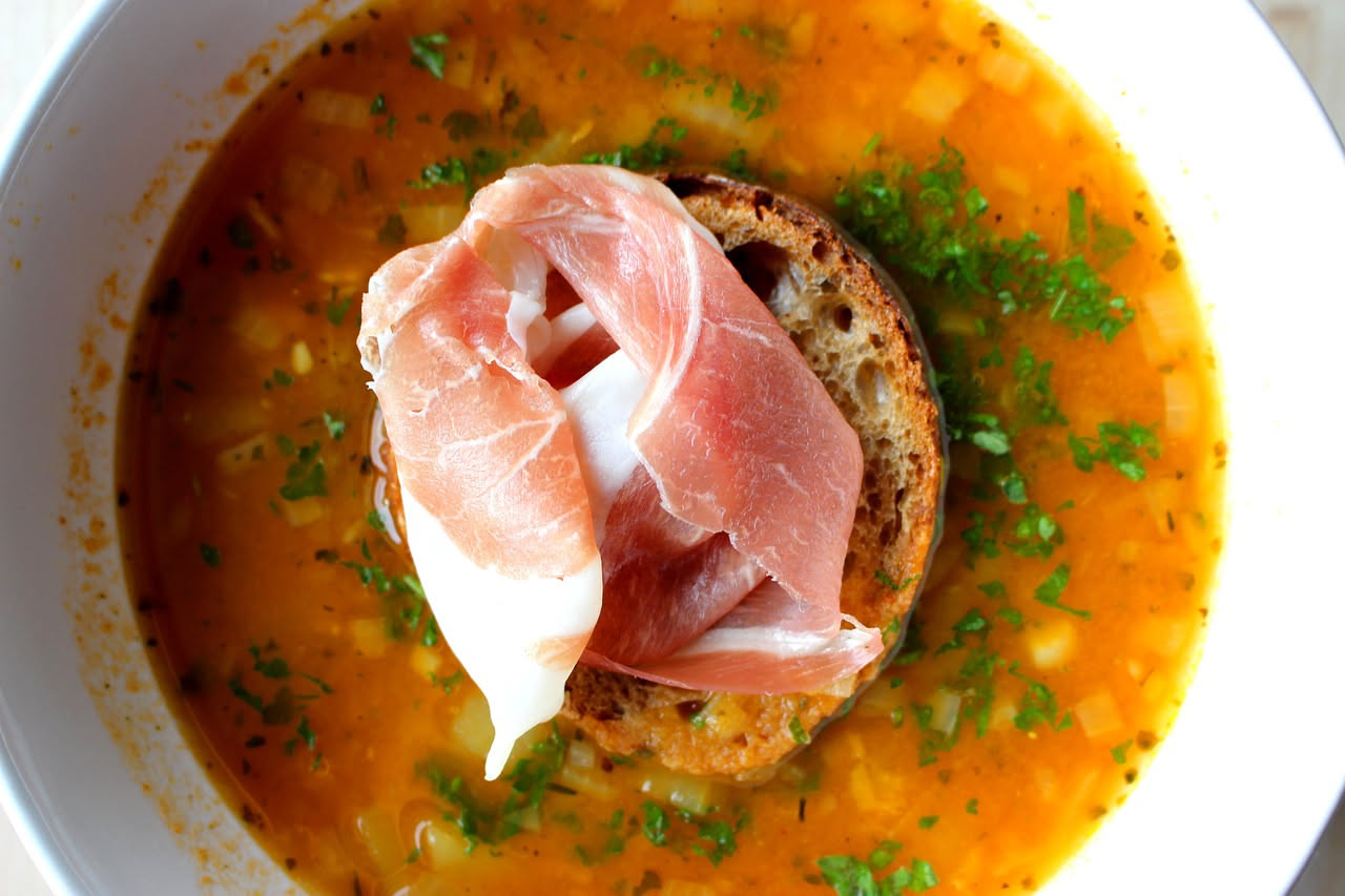 Ciotola di ceramica con acquacotta fumante: zuppa scura con verdure, fette di pane tostato e tuorlo d'uovo visibile, servita su tavolo rustico di legno