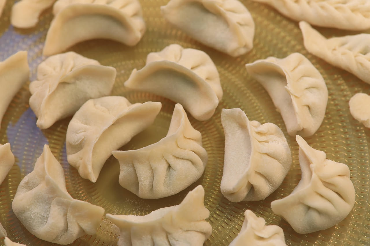 Agnolotti di carne quadrati e leggermente gonfi in un piatto bianco immersi in brodo trasparente color ambra, guarniti con una noce di burro e parmigiano grattugiato, filo di prezzemolo fresco