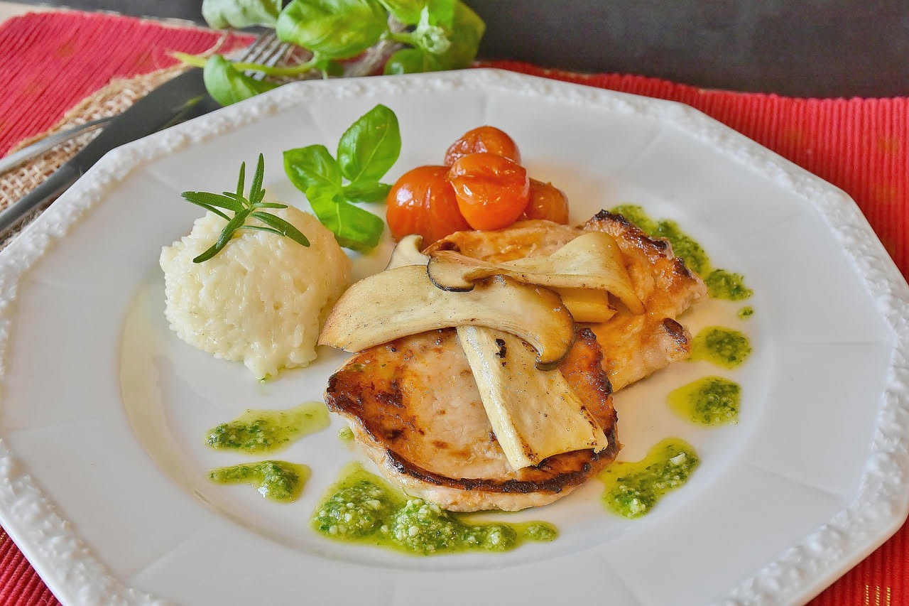 Anguilla cotta in un piatto fondo bianco, circondata da verdure soffritte color ambra e cipolla caramellata, brodo ricco che copre la base del piatto, prezzemolo fresco sopra