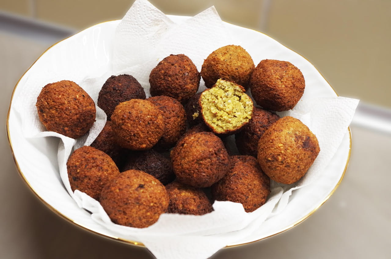 Tre arancini di melanzane tondi, dorati e croccanti, disposti su un piatto bianco con contorno di pomodori freschi e basilico verde