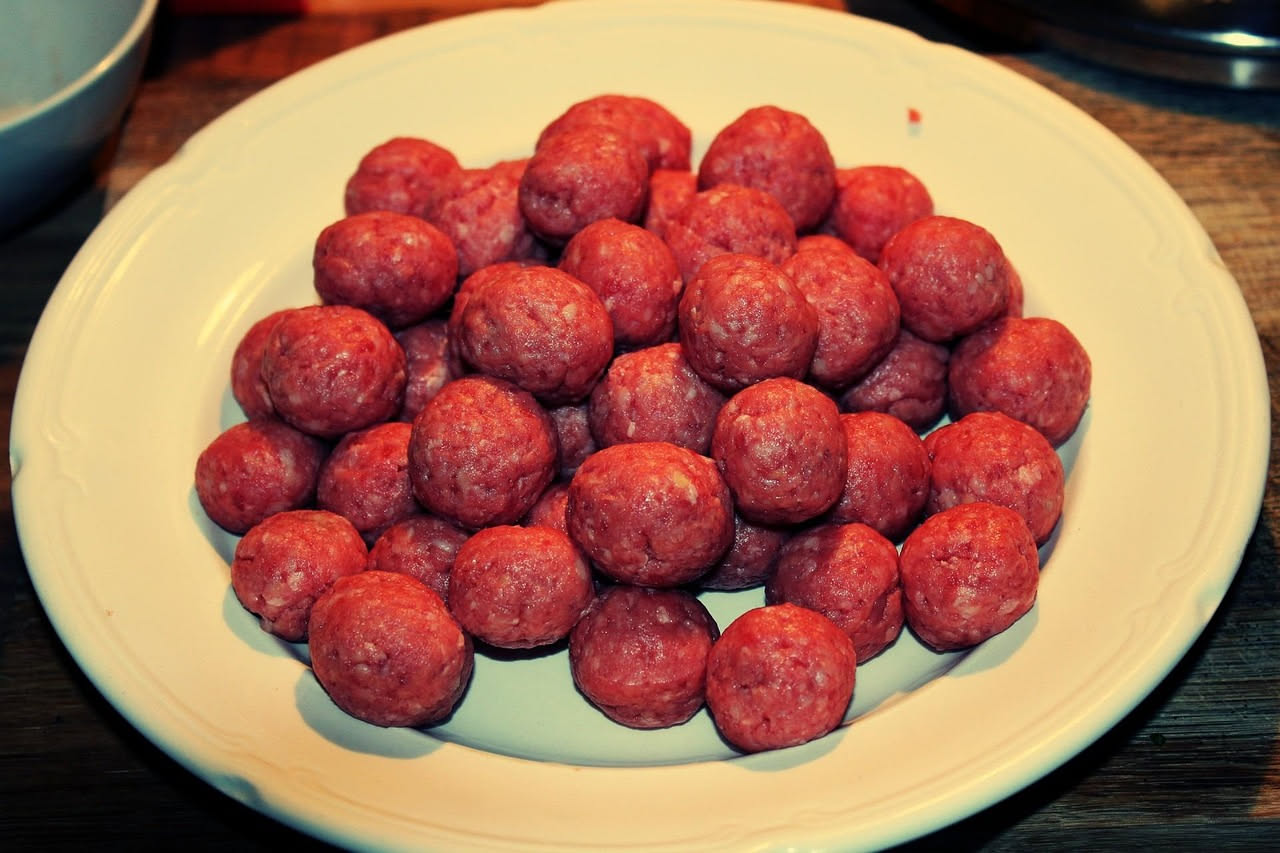 Tre arancini di ragù dorati e croccanti appoggiati su carta bianca, uno tagliato a metà che mostra il ripieno di ragù e formaggio filante all'interno, con una ciotola di ragù sfocata sullo sfondo