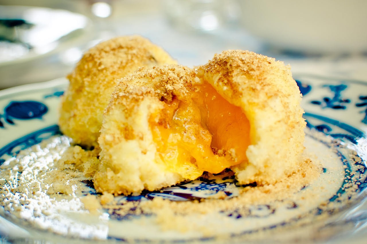 Tre arancini marchigiani dorati e croccanti disposti su un piatto bianco, tagliato uno in due per mostrare il ragù interno e la mozzarella filante, con sedano e carota accanto