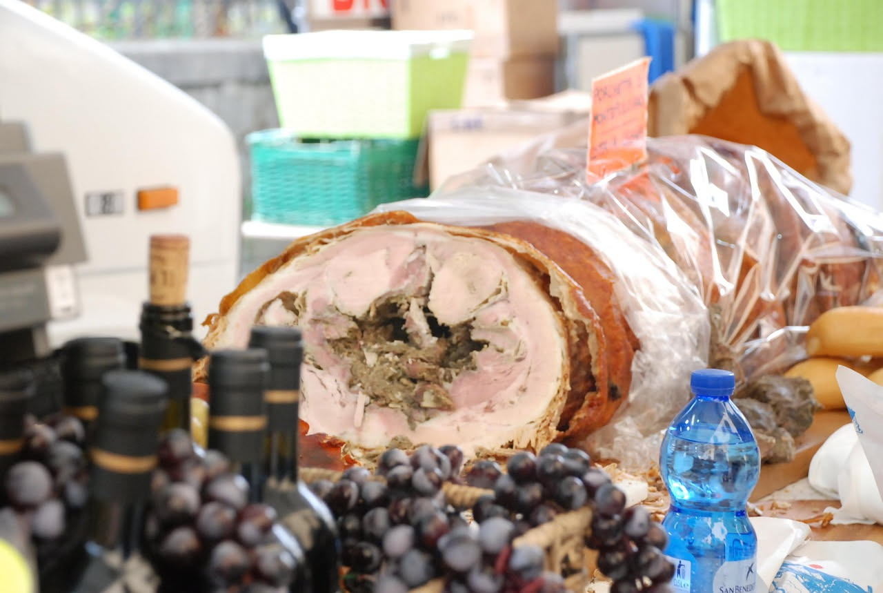 Arista in crosta appena sfornata, dorata e croccante, tagliata a fette spesse che lasciano intravedere la carne rosa tenera all'interno, contornata da erbe di rosmarino fresco