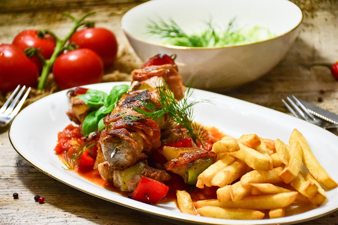 Arrosticinelli dorati e croccanti in fila su un piatto bianco, cotti alla griglia, con sfumature brunastre sulla superficie, accompagnati da limone fresco e prezzemolo