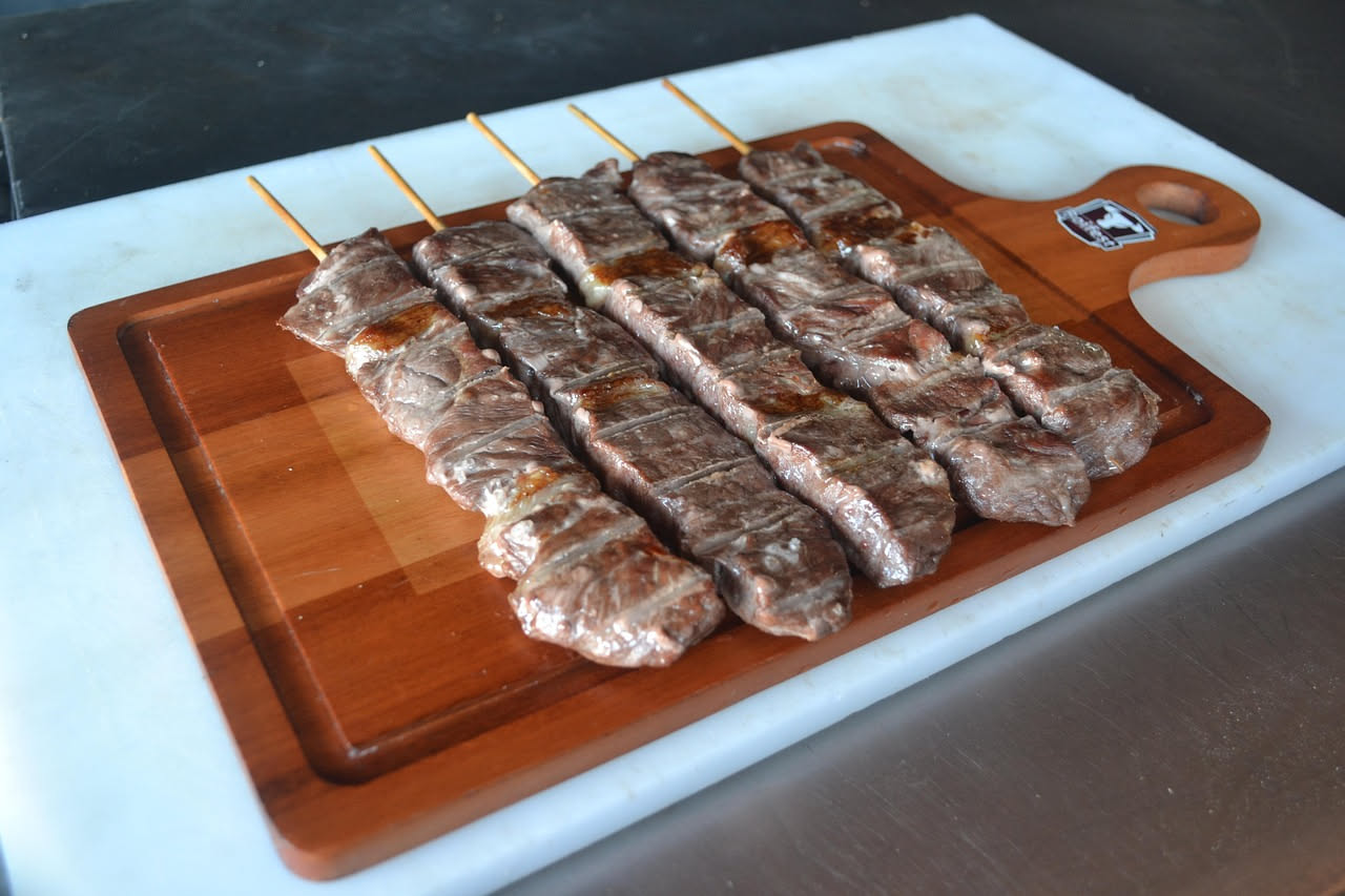Arrosticini di cavallo rosati e dorati grigliati, disposti su un piatto bianco con fette di limone, sale grosso e prezzemolo fresco, fiamma viva sullo sfondo