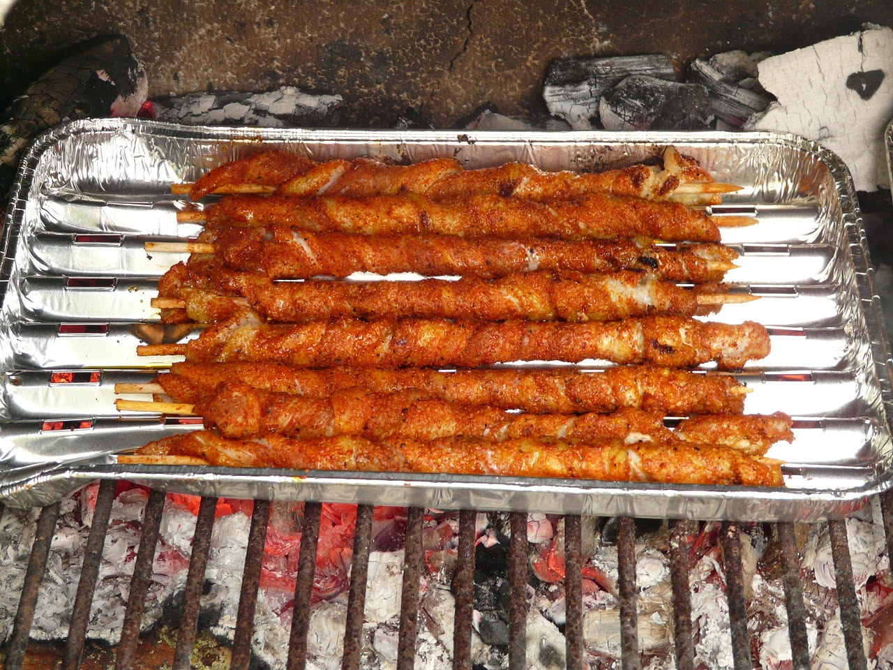 Arrosticini leccesi appena cotti su una piastra nera, con cubetti di carne rossa dorata e pezzi di peperone rosso e cipolla, conditi con olio verde scuro