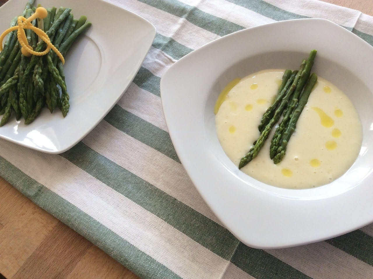 Asparagi verdi disposti verticalmente su un piatto bianco, ricoperti di burro fuso lucido e scaglie dorate di parmigiano stagionato