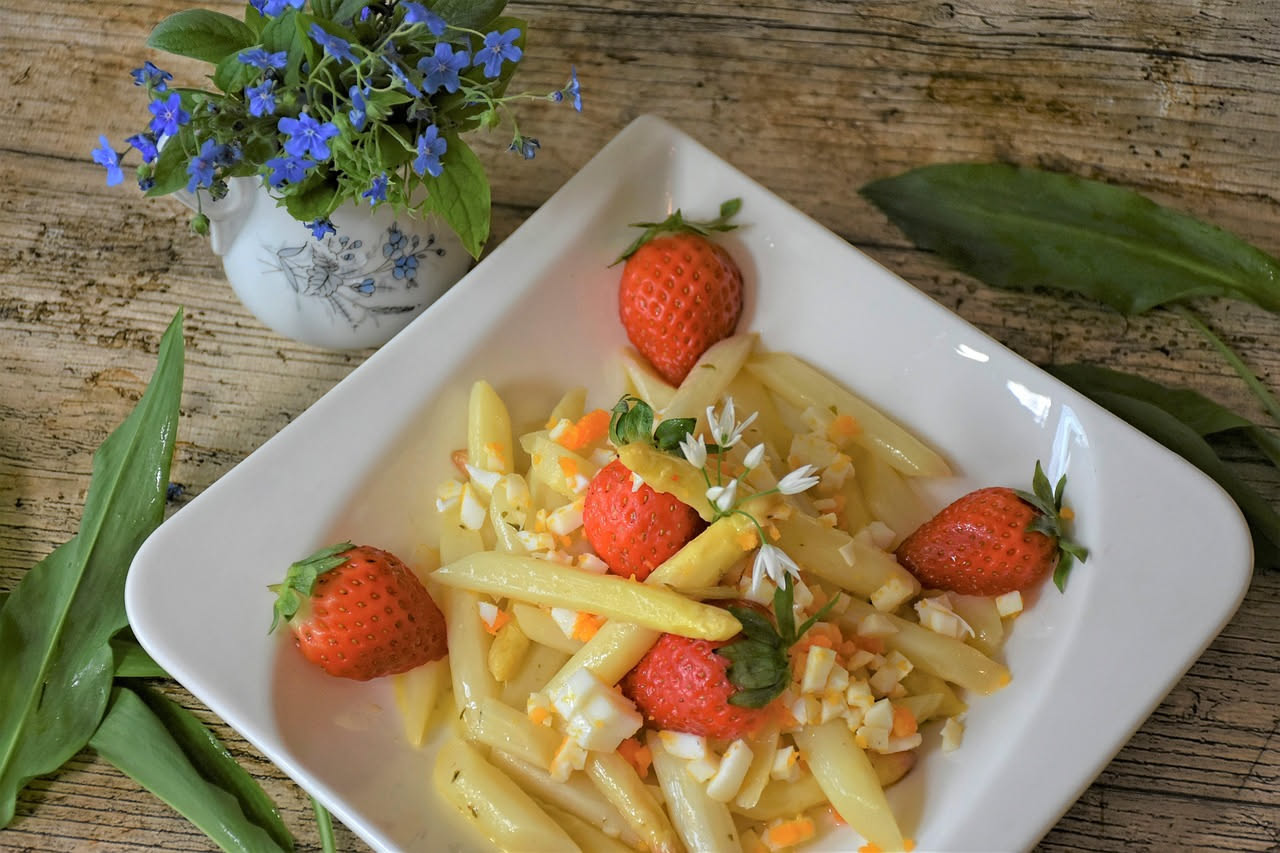 Asparagi di montagna sottili e verdissimi, saltati in padella, con aglio dorato e olio lucido, disposti a ciuffo su un piatto bianco, con limone fresco a spicchi sul bordo