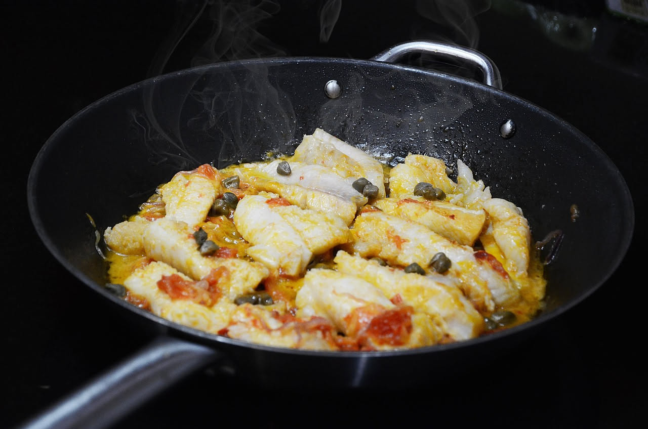 Piatto di baccalà in umido con pomodori rossi, olive nere e peperoni gialli, servito in una ciotola di ceramica con pane accanto