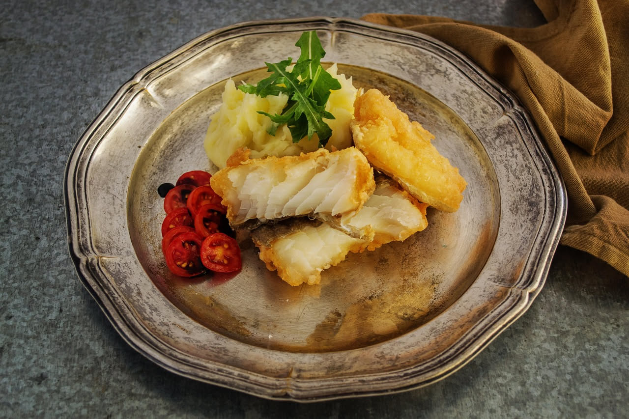 Baccalà in insalata in una ciotola di ceramica bianca: filetti di pesce bianco, pomodorini rossi, cipolla rossa affettata, olive nere, prezzemolo fresco verde