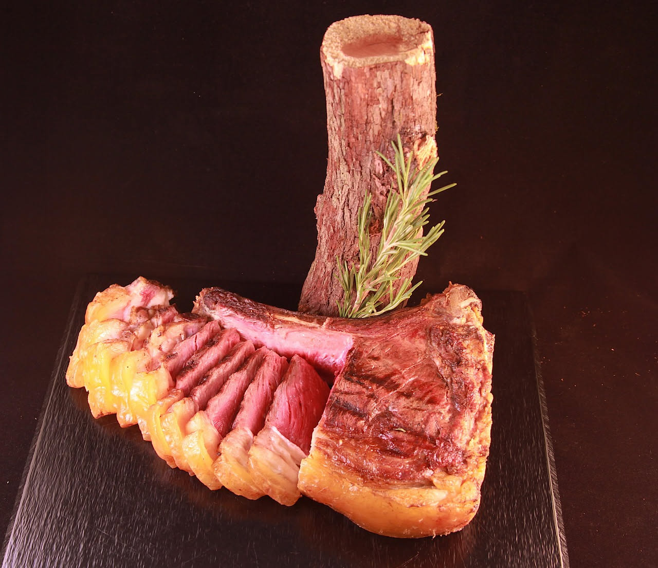 Una bistecca alla fiorentina da due centimetri di spessore, con crosta marrone scuro e interno rosa acceso, cosparsa di sale e posata su un piatto bianco con fette di limone fresco ai lati