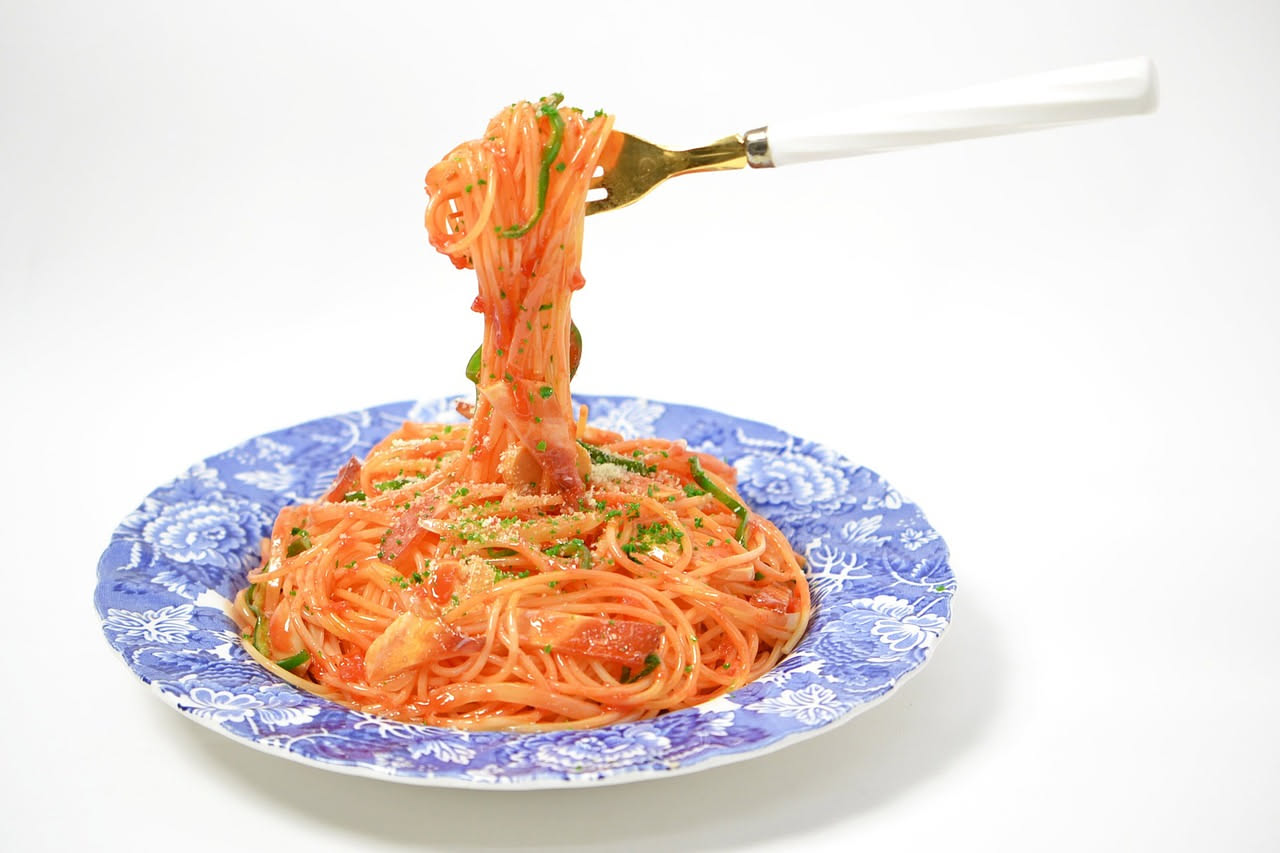 Bottarga di muggine intera color ambra scuro accanto a una grattugia in metallo, con pezzetti di bottarga grattugiata sparsi su un piatto bianco e qualche filo sul fondo