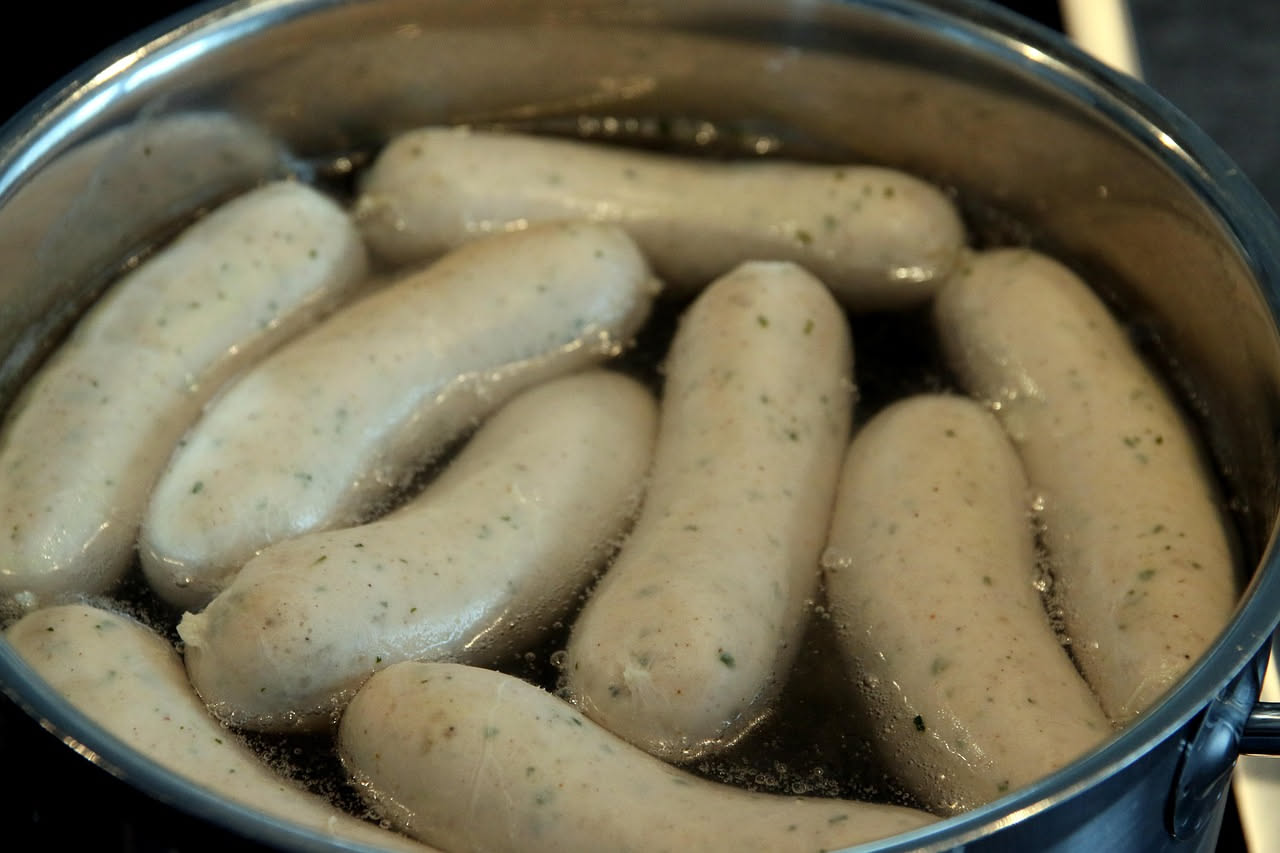 Boudins scuri e lucidi disposti nel piatto bianco, contornati da fette di mela gialla e cipolla caramellata, vapore ancora visibile dalla superficie