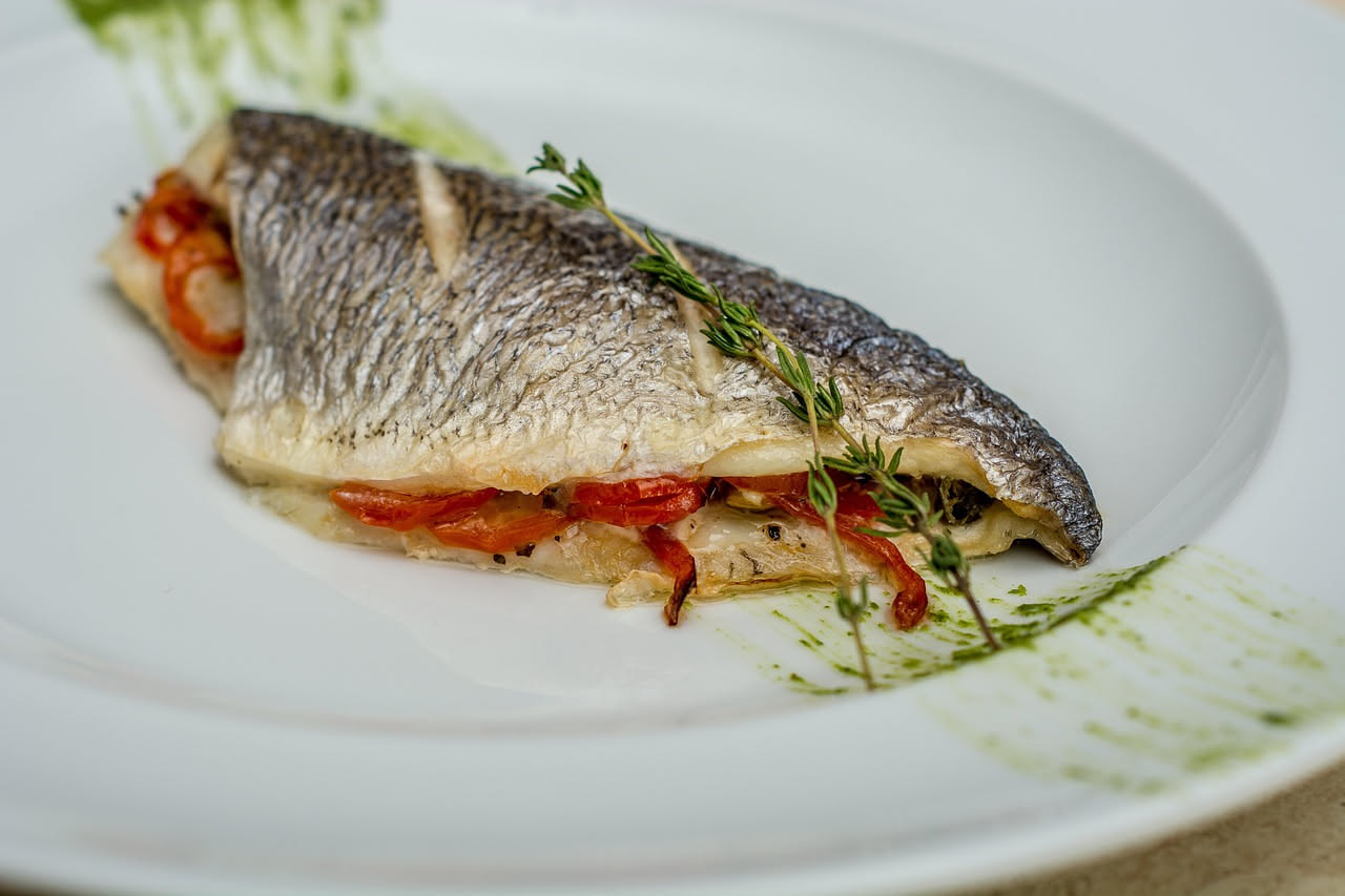 Filetti di branzino marinato trasparenti con limone fresco affettato, olio d'oliva e prezzemolo verde in piatto bianco