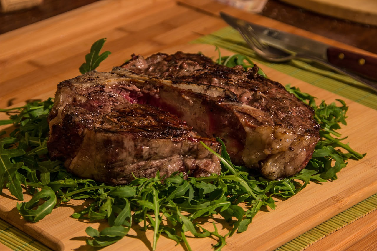Fette sottili di manzo rosa e marrone di brazzata vicentina disposte a ventaglio su un piatto bianco, con contorno di verdure lesse e salsa verde.