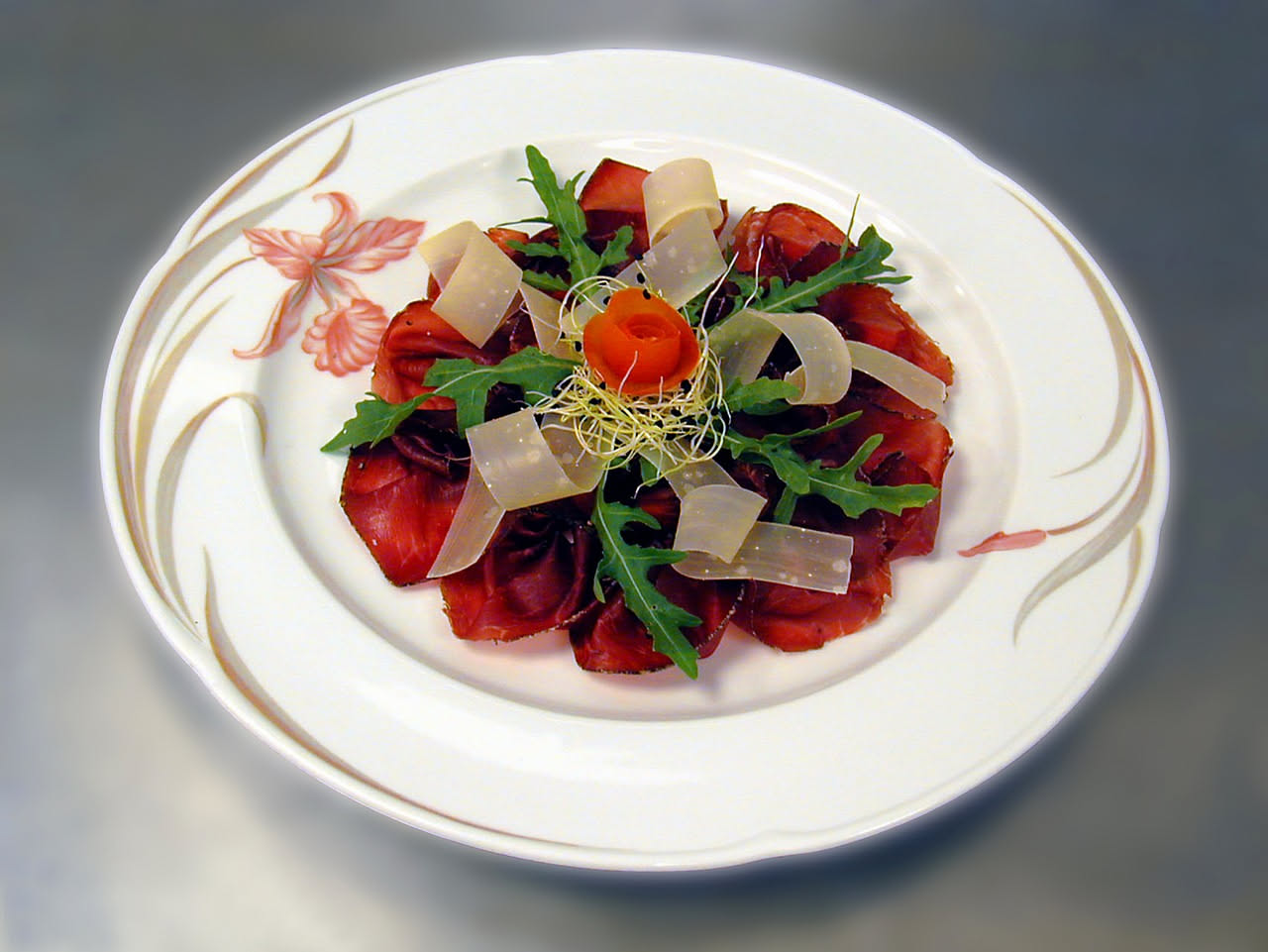 Fette di bresaola di Modena rosso scuro affettate sottili su un piatto bianco, con gocce di olio d'oliva e pepe nero, accanto pane tostato