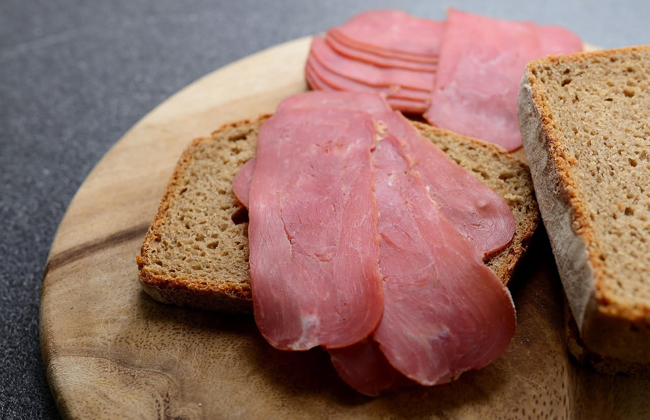 Fette sottili di bresaola trentina rosa scuro disposte a ventaglio su piatto bianco, condite con gocce di olio d'oliva verde chiaro e una spruzzata di pepe nero macinato fresco