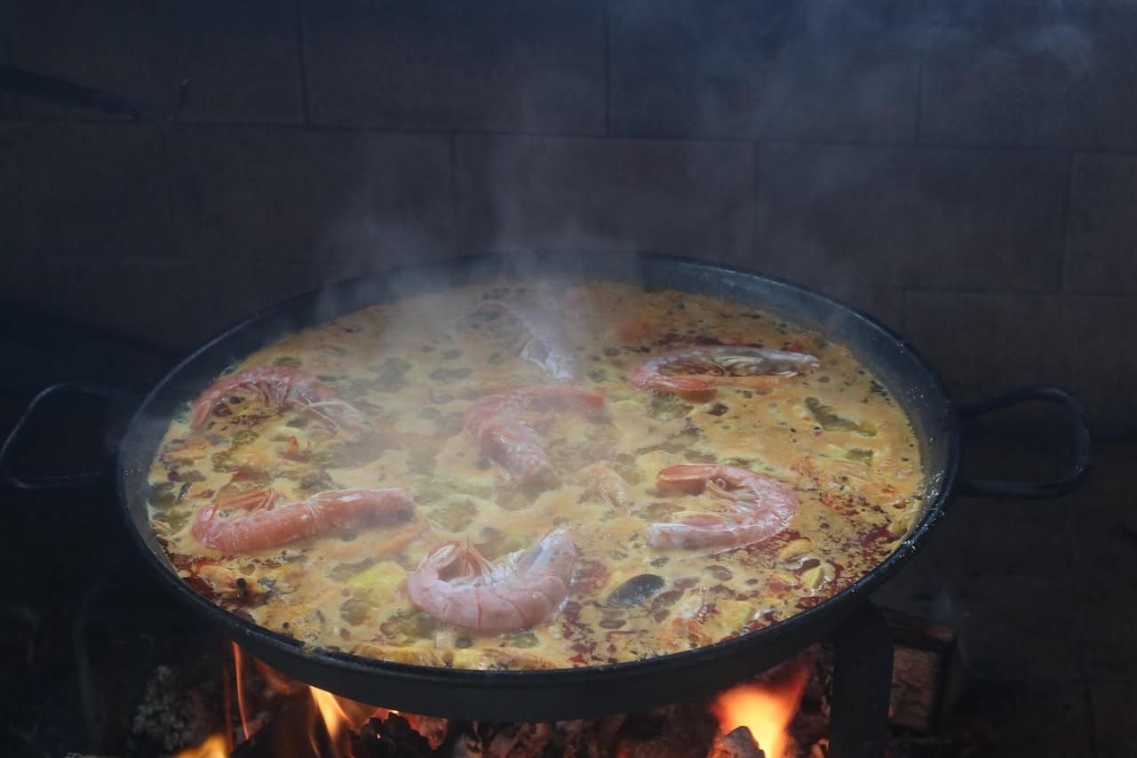 Zuppa di pesce in ciotola bianca con pezzi di pesce bianco, pomodori rossi, cipolla, accompagnata da fette di pane tostato scuro, posta su tavolo di legno con tovaglia lino beige, fiasco di olio d'oli