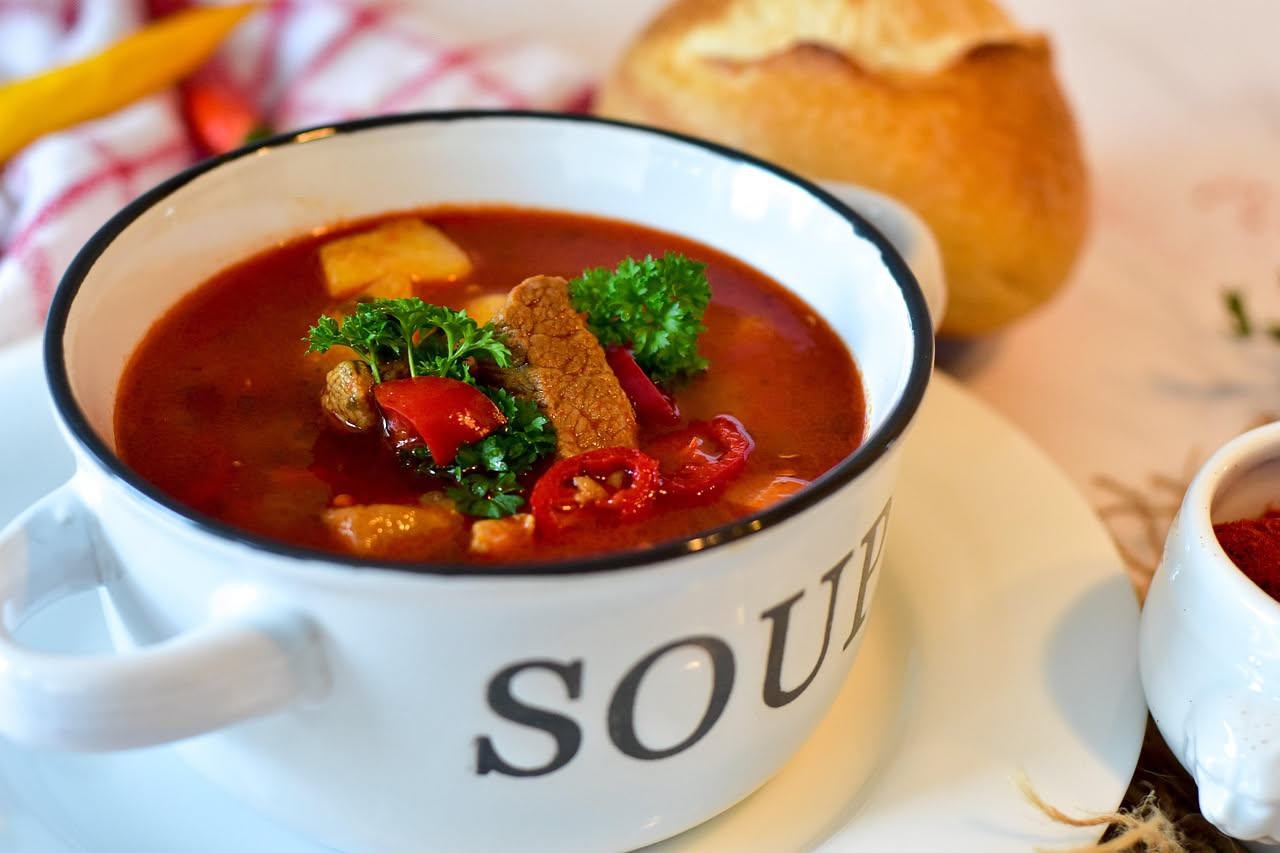 Zuppa di brodetto alla grossetana in ciotola bianca con pezzi di polpo, moscardini bianchi, brodo rosso e salsa di pomodoro, con fette di pane tostato a lato