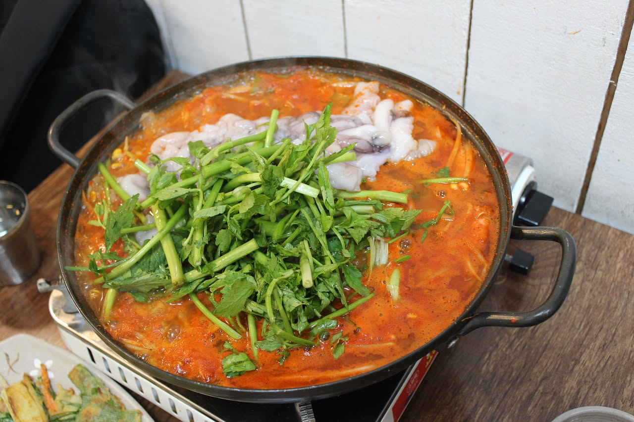 Una ciotola di ceramica bianca con brodetto di moscardini: molluschi piccoli e tenerissimi immersi in un brodo rosso intenso di pomodoro, con fette di pane tostato accanto, erbe verdi di prezzemolo fr