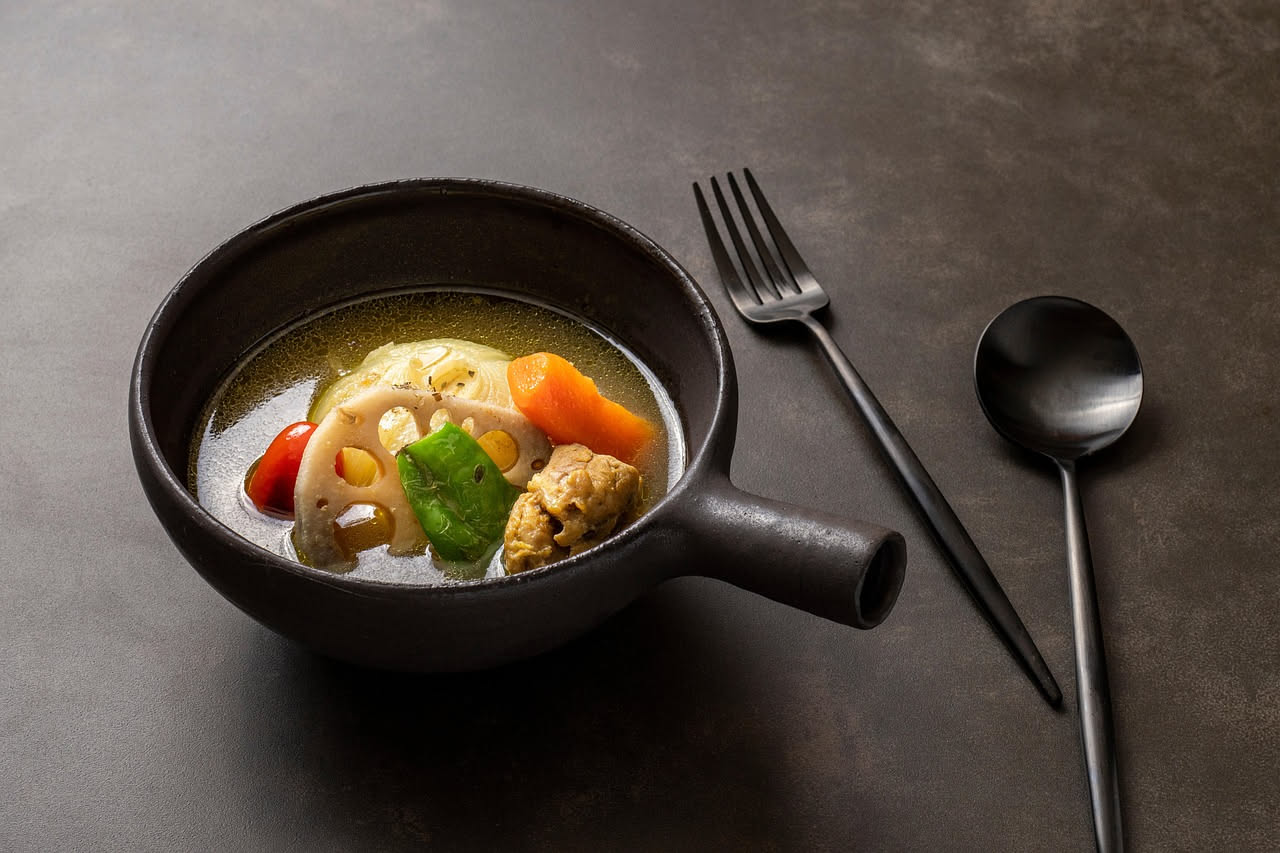 Brodetto di verdure in una ciotola bianca: brodo trasparente e fragrante con cubetti di carote arancioni, sedano verde, zucchine chiare, pomodoro rosso, prezzemolo fresco sulla superficie, servito su