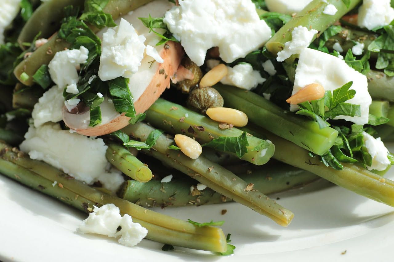 Bruscandoli verdi e croccanti in padella con aglio dorato, olio di oliva lucente, limone fresco a fette sul bordo, serviti su piatto bianco con cucchiaio di legno