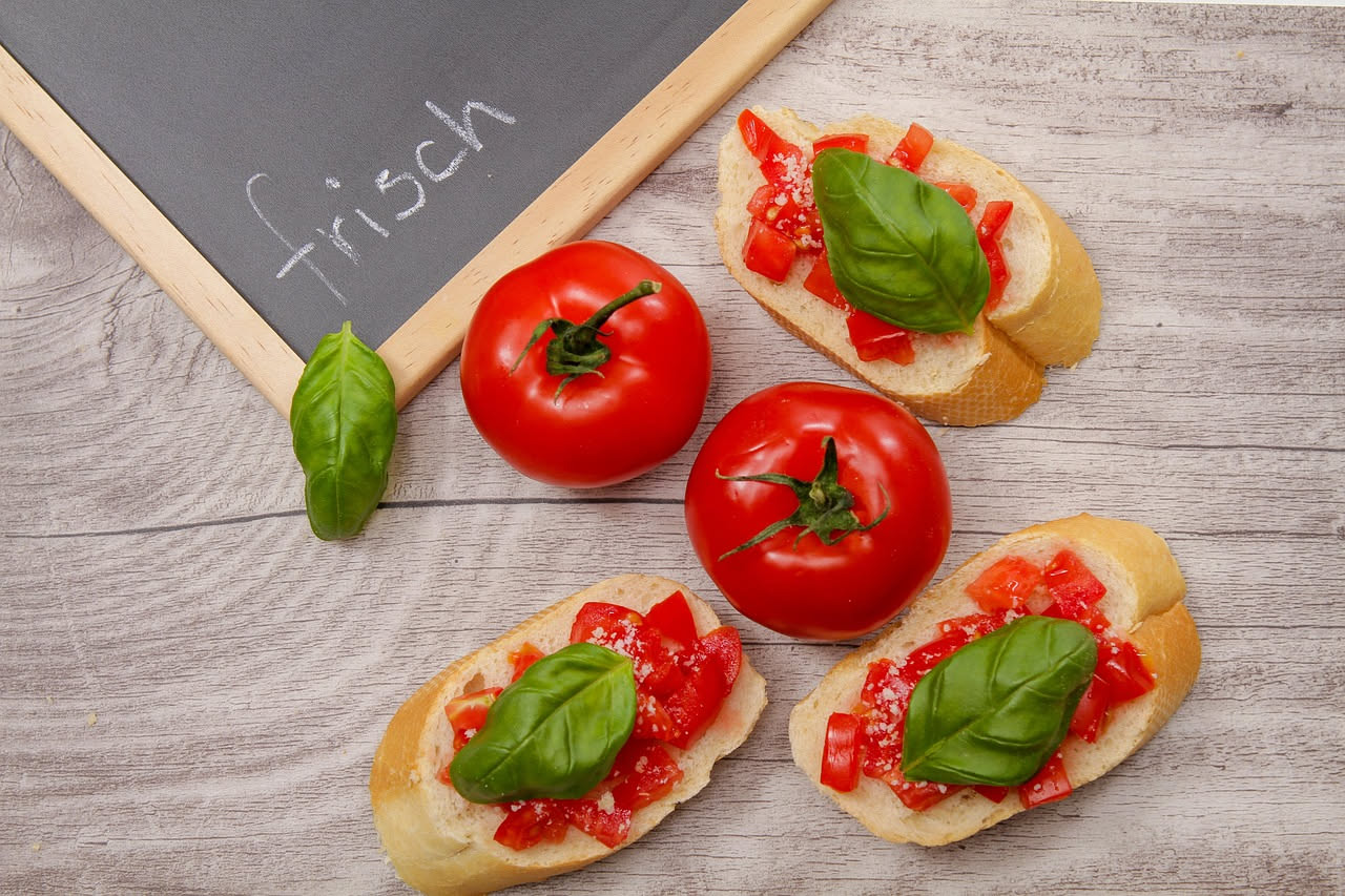 Bruschettas con pane tostato croccante, condimento rosso di pomodori freschi e foglie verdi di basilico su un piatto bianco