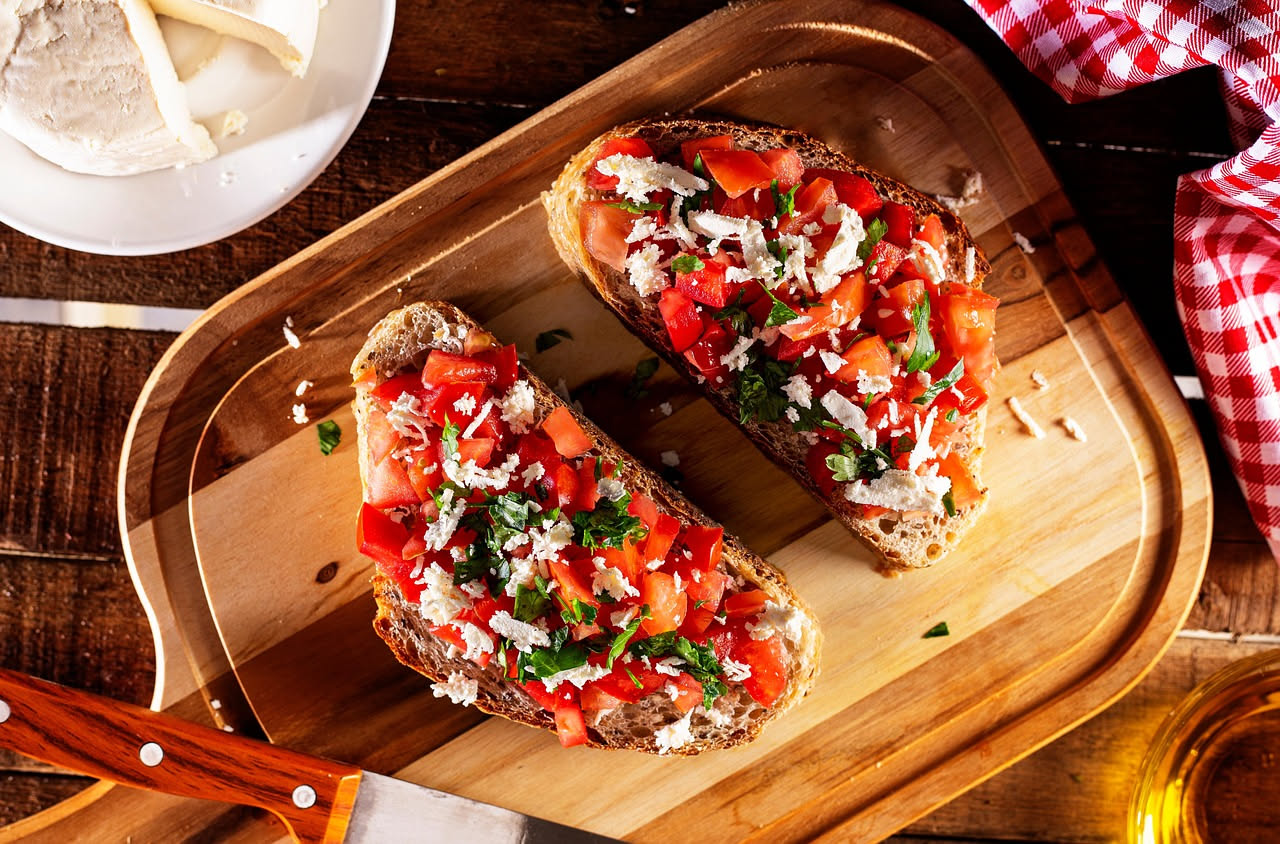 Tre bruschette su piatto bianco con fette di pane tostato dorate e croccanti, coperte da uno strato di formaggio color avorio leggermente dorato, guarnite con erba cipollina e pepe nero macinato fresc