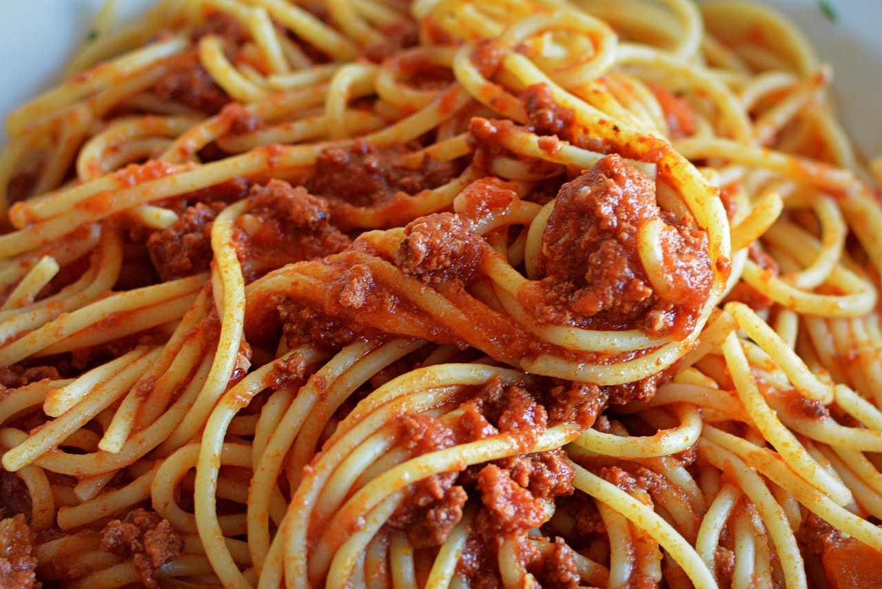 Piatto di bucatini al ragù di pesce spada: pasta riccioluta ricoperta di sugo scuro e corposo, con frammenti visibili di pesce bianco, condito con prezzemolo fresco tritato, in piatto bianco fondo su
