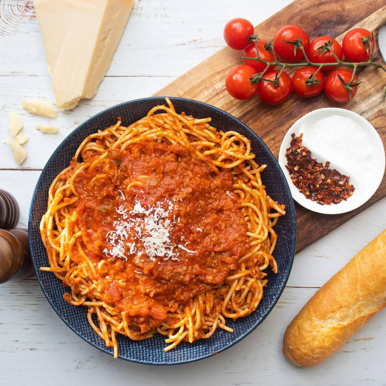 Piatto bianco con bucatini all'amatriciana, pasta lunga sottile con salsa rossa brillante, guanciale croccante marrone dorato, grana di pecorino bianca e punte di peperoncino rosso, tovaglia bianca