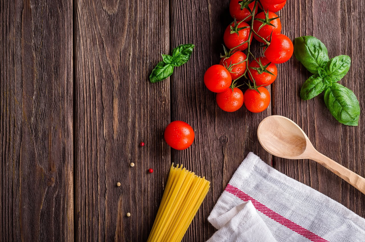 Piatto di bucatini con salsa rossa a base di pomodori, mandorle tostate visibili sulla pasta, basilico fresco verde, servito su piatto bianco con olio di oliva colato sopra