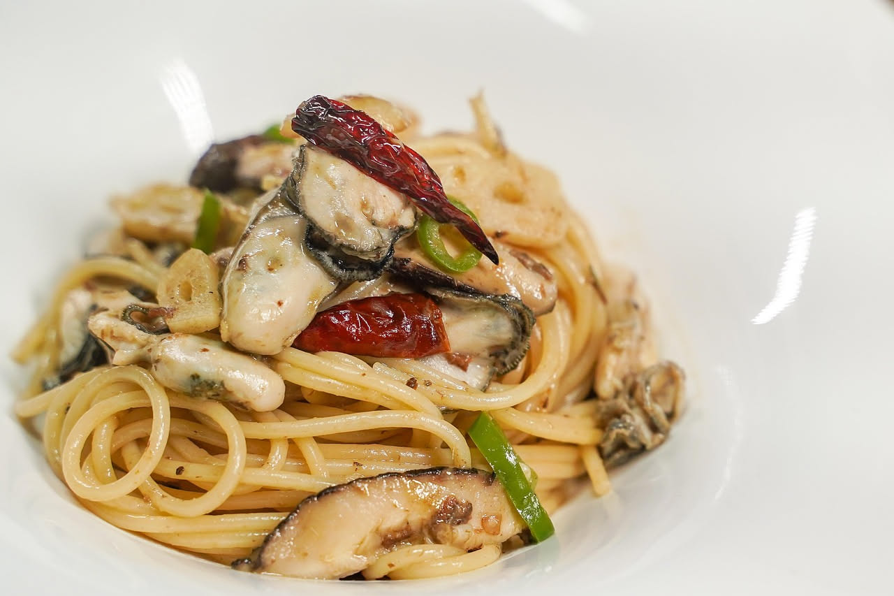 Piatto di bucatini alle cozze: pasta lunga con dentro cozze aperte nere e blu, ricoperta di salsa rossa di pomodoro e aglio, decorato con prezzemolo verde fresco