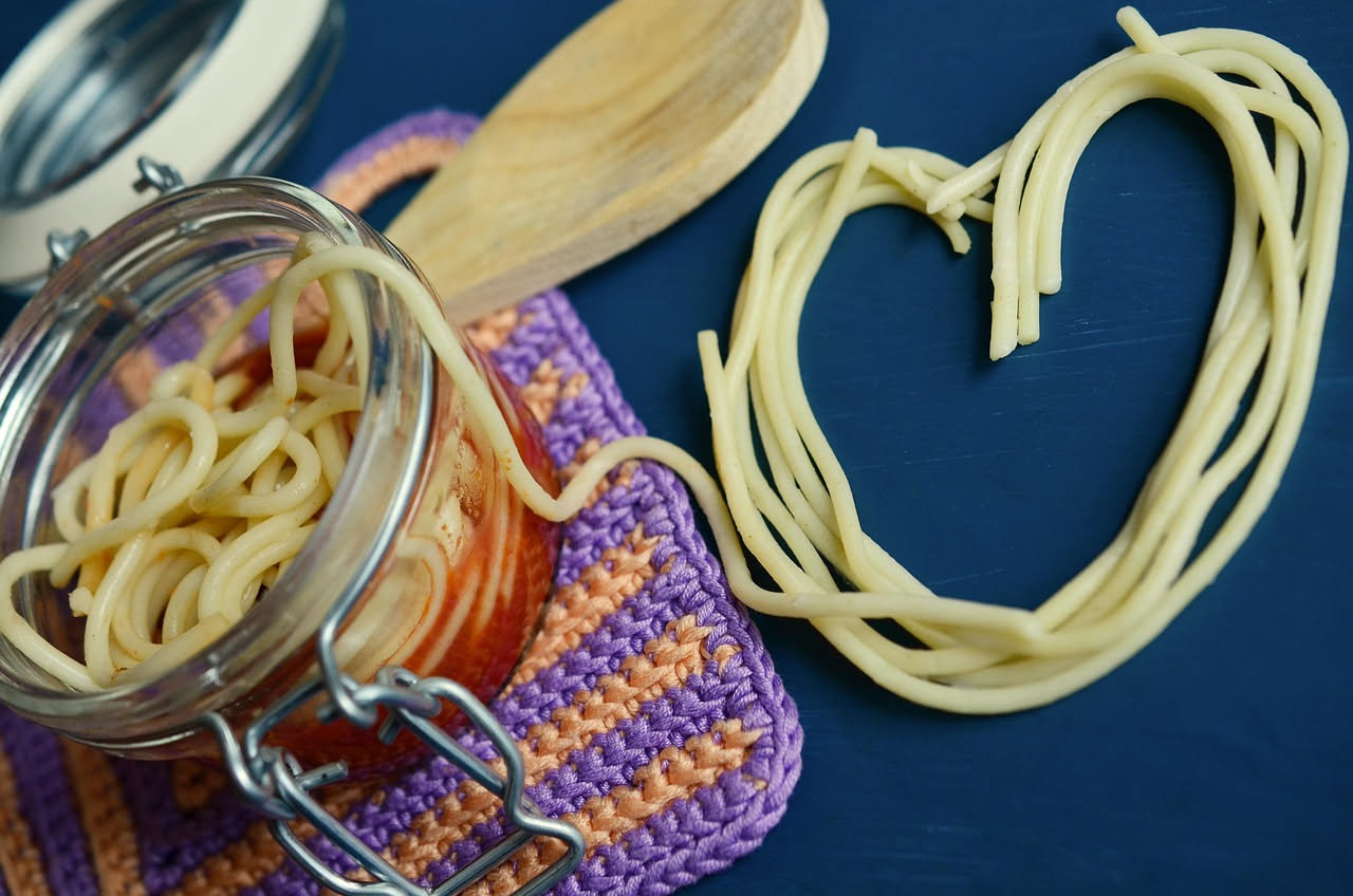 Piatto fondo bianco con bucatini conditi da alici intere, aglio dorato, prezzemolo fresco e gocce di olio verdastro, pasta al dente con filo di peperone rosso macinato