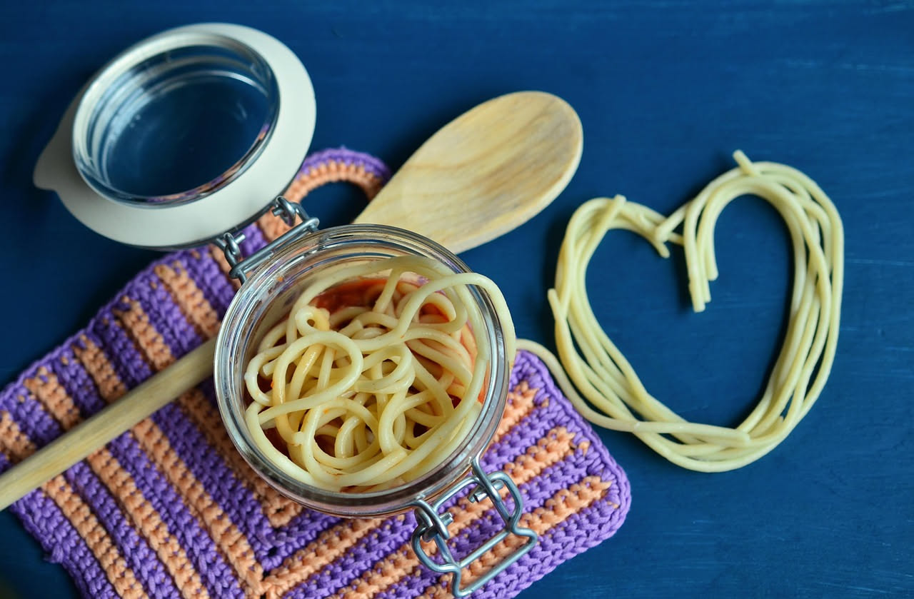 Buccatini al tonno in piatto bianco: pasta di colore giallo-dorato avvolta intorno alla forchetta, sugo rosso con pezzetti di tonno bianco, prezzemolo fresco verde, filo di olio d'oliva che luccica, s