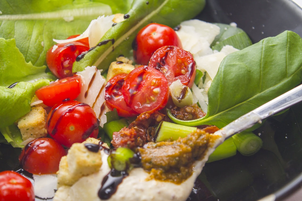 Burrata bianca e cremosa al centro del piatto con intorno pomodori rossi e gialli tagliati a spicchi, basilico fresco e gocce di olio verde in superficie su sfondo bianco
