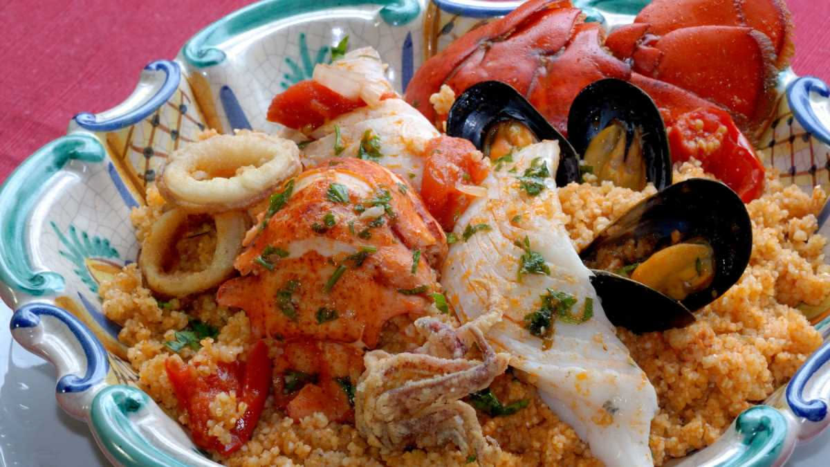 Zuppa di pesce caciucco in ciotola bianca con polpo, vongole e brodo scuro, servita con pane tostato a lato e erbe fresche di prezzemolo