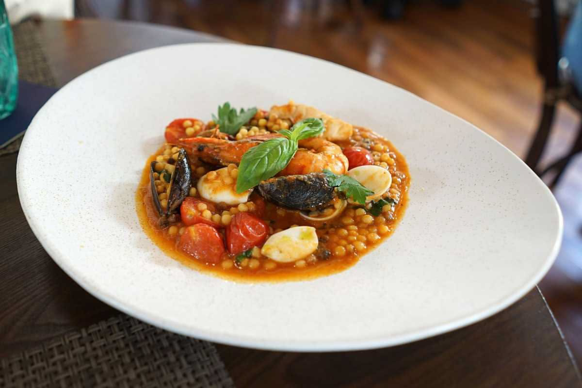 Zuppa di pesce in terracotta con calamari, vongole, gamberi e branzino in brodetto rosso, pane tostato appoggiato sul bordo