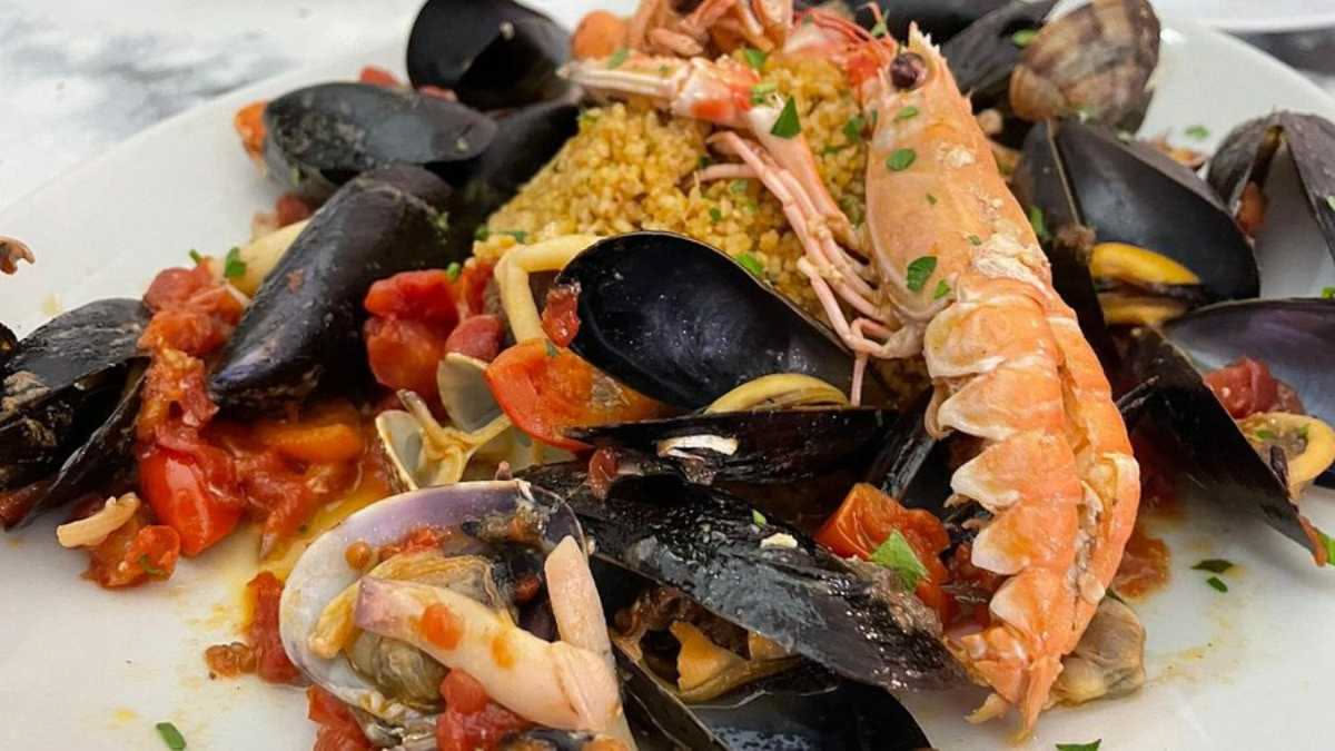 Zuppa di pesce caciucco in ciotola di terracotta con polpo, gamberi, cozze, scorfano e brodetto rosso con fette di pane tostato a lato