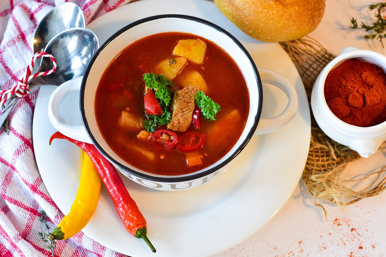 Ciotola di caciucco marchigiano con brodo rosso-arancione, pezzi di pesce bianco, cozze aperte, vongole, pomodori, servito su fette di pane tostato grigio, con pepe nero e prezzemolo verde in superfic