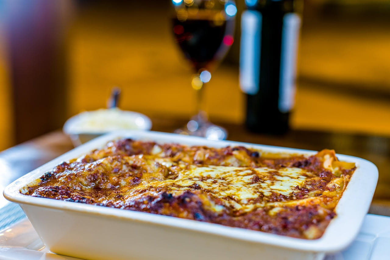 Cannelloni siciliani appena sfornati, disposti in fila in una pirofila bianca, ricoperti di besciamella color crema, formaggio dorato gratinato in superficie, vapore visibile appena escono dal forno