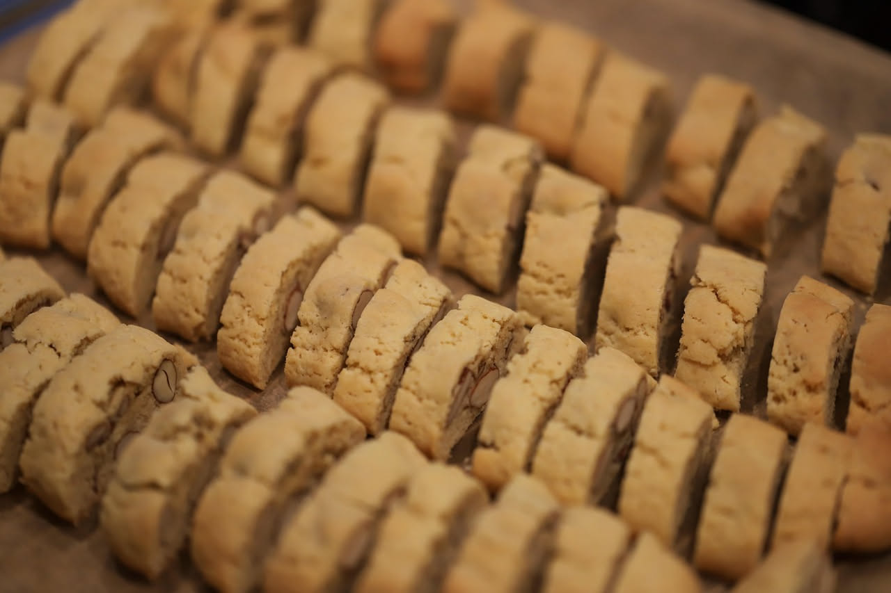 Cantuccini salati croccanti disposti su una tavola di legno, con mandorle intere visibili, accanto a un bicchiere di vino bianco
