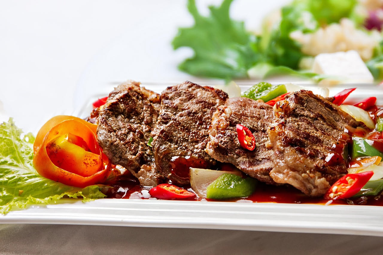 Tre involtini di carne alla messinese adagiati su un piatto bianco con sugo di pomodoro rosso scuro, cipolle dorate intorno e un cucchiaio di sugo sul bordo