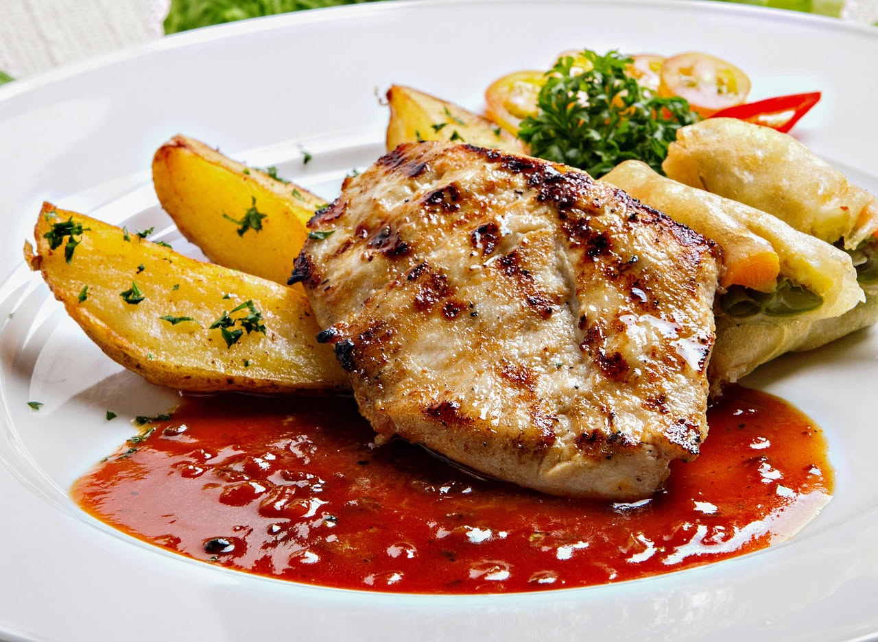 Fettine di carne marrone dorate in padella con sugo rosso acceso di pomodori, aglio e prezzemolo fresco, cipolla trasparente attorno, piatto di ceramica bianca con contorno di insalata verde