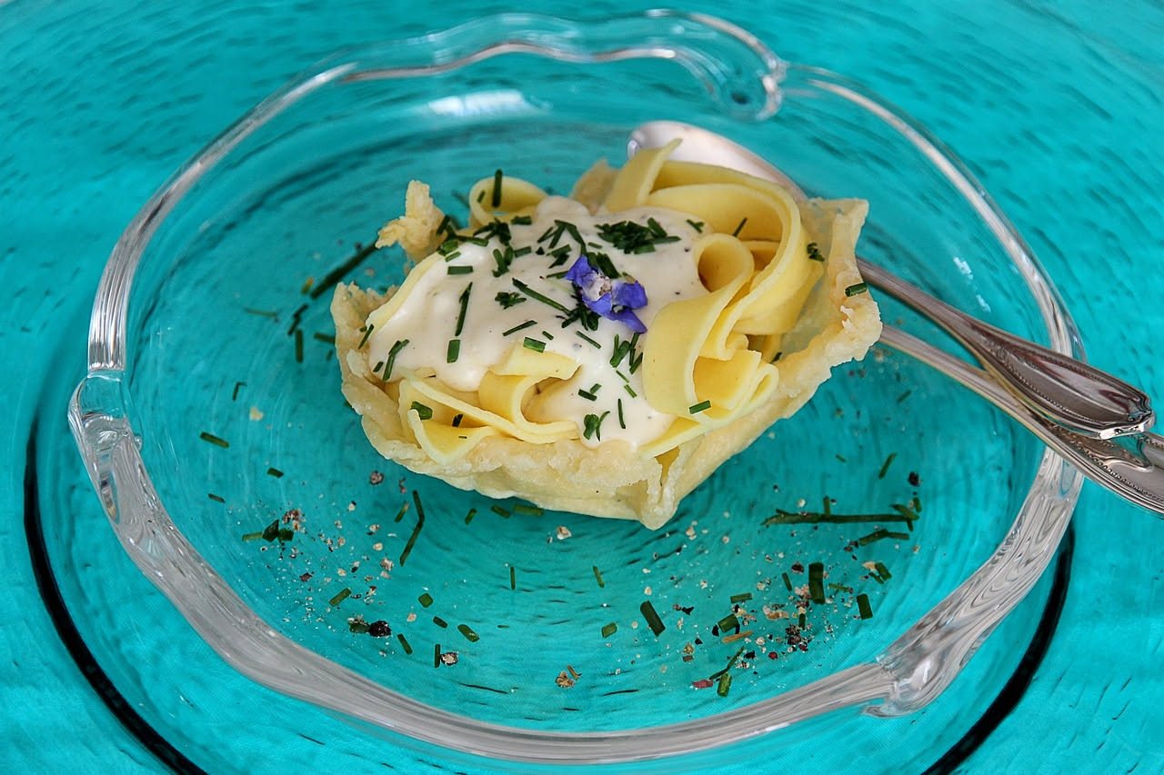 Cartellate salate dorate a forma di rosa impilate su un piatto bianco, cosparse di formaggio grattugiato e pepe nero, con erbette aromatiche sparse intorno