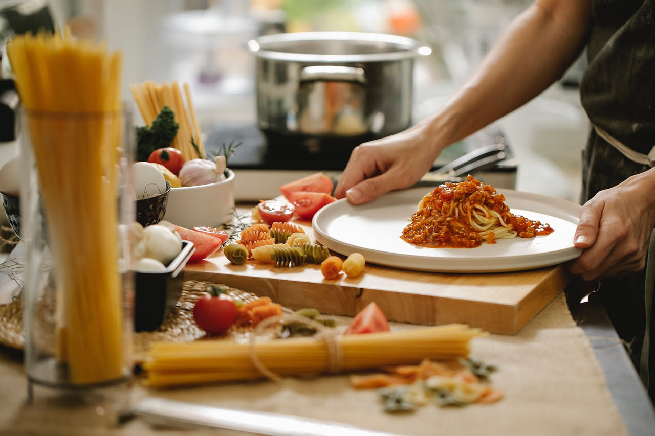 Piatto di casarecce al ragù calde con sugo di carne rosso scuro, spolverato di parmigiano grattugiato bianco, accompagnato da un bicchiere di vino rosso su tavolo in legno