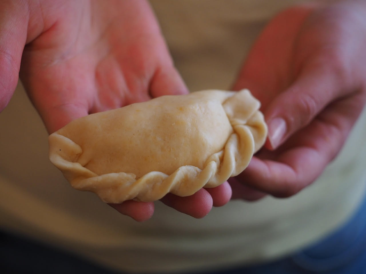 Casunziei dolci dorati, a forma di mezzaluna panciuta, disposti nel piatto bianco con burro fuso colato sopra e zucchero semolato sparso, su sfondo di legno scuro